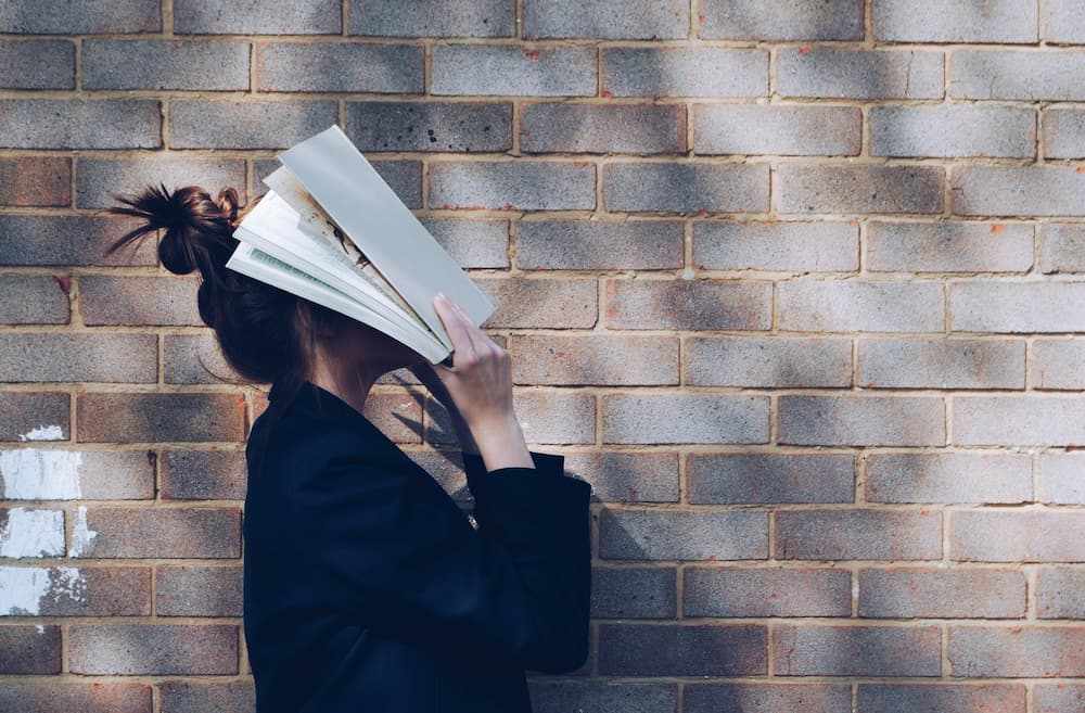 Estudiante frustrada ocultándose tras un libro, relacionada con la ley de ausentismo escolar.