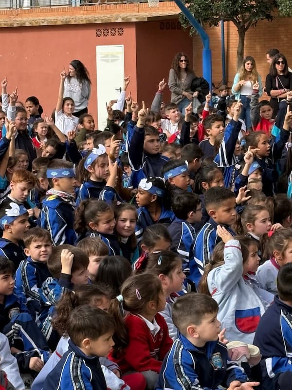 Niños del colegio sentados con cintas azules en la cabeza cantando durante el Día de la Paz colegio.